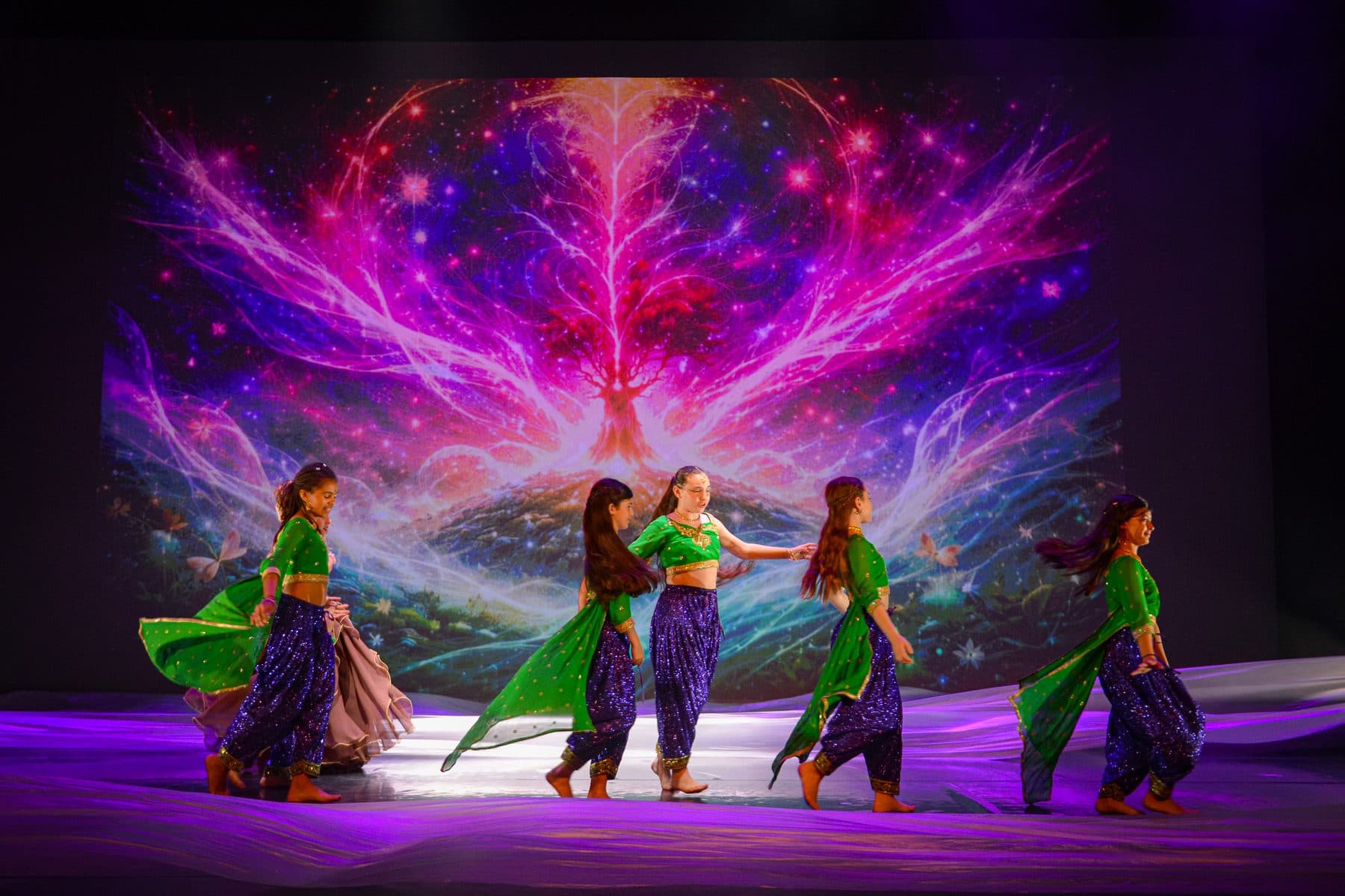 Danseuses en costumes chatoyants devant une projection de nébuleuse colorée
